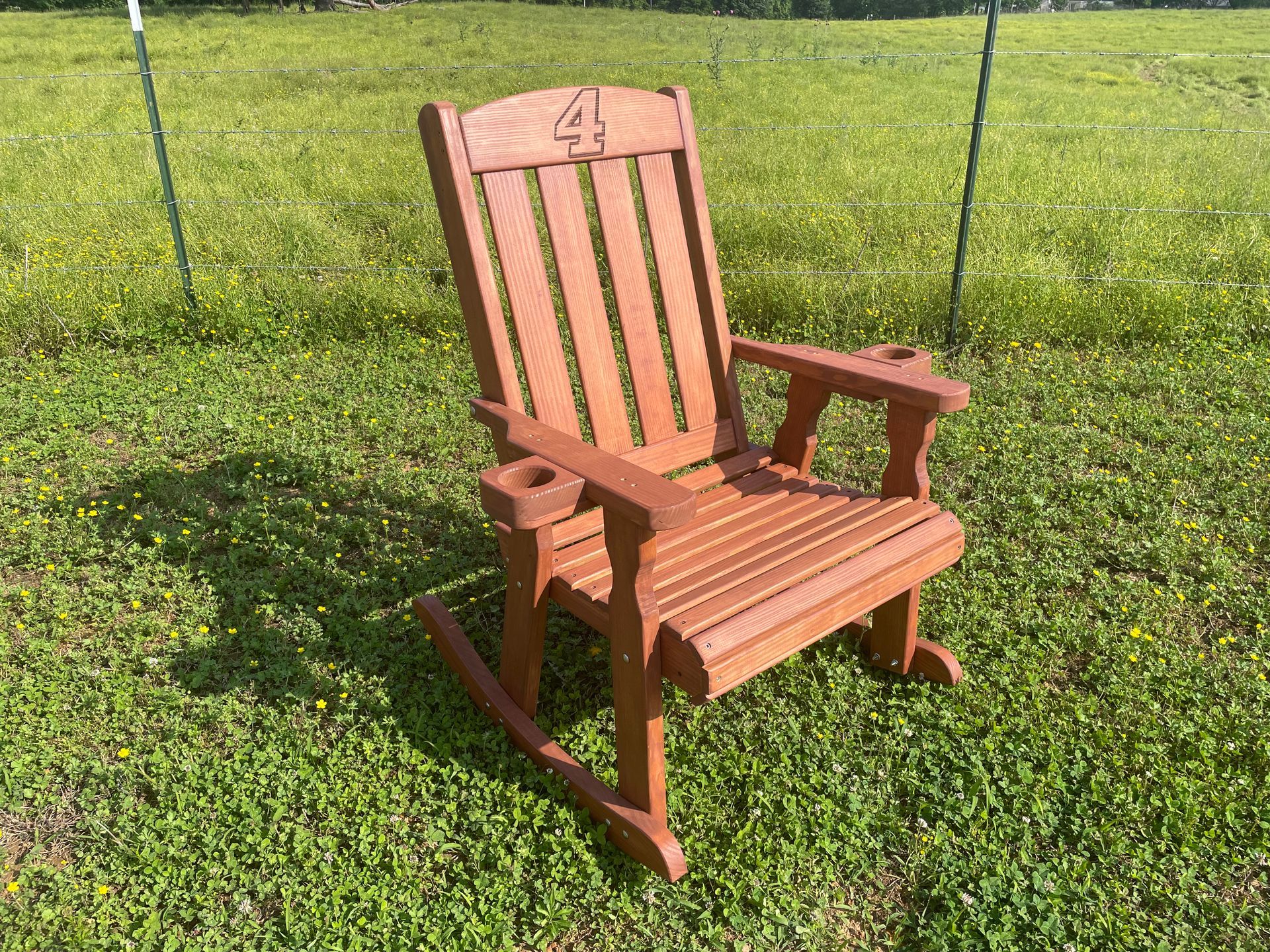 A wooden rocking chair is sitting in the grass in a field.