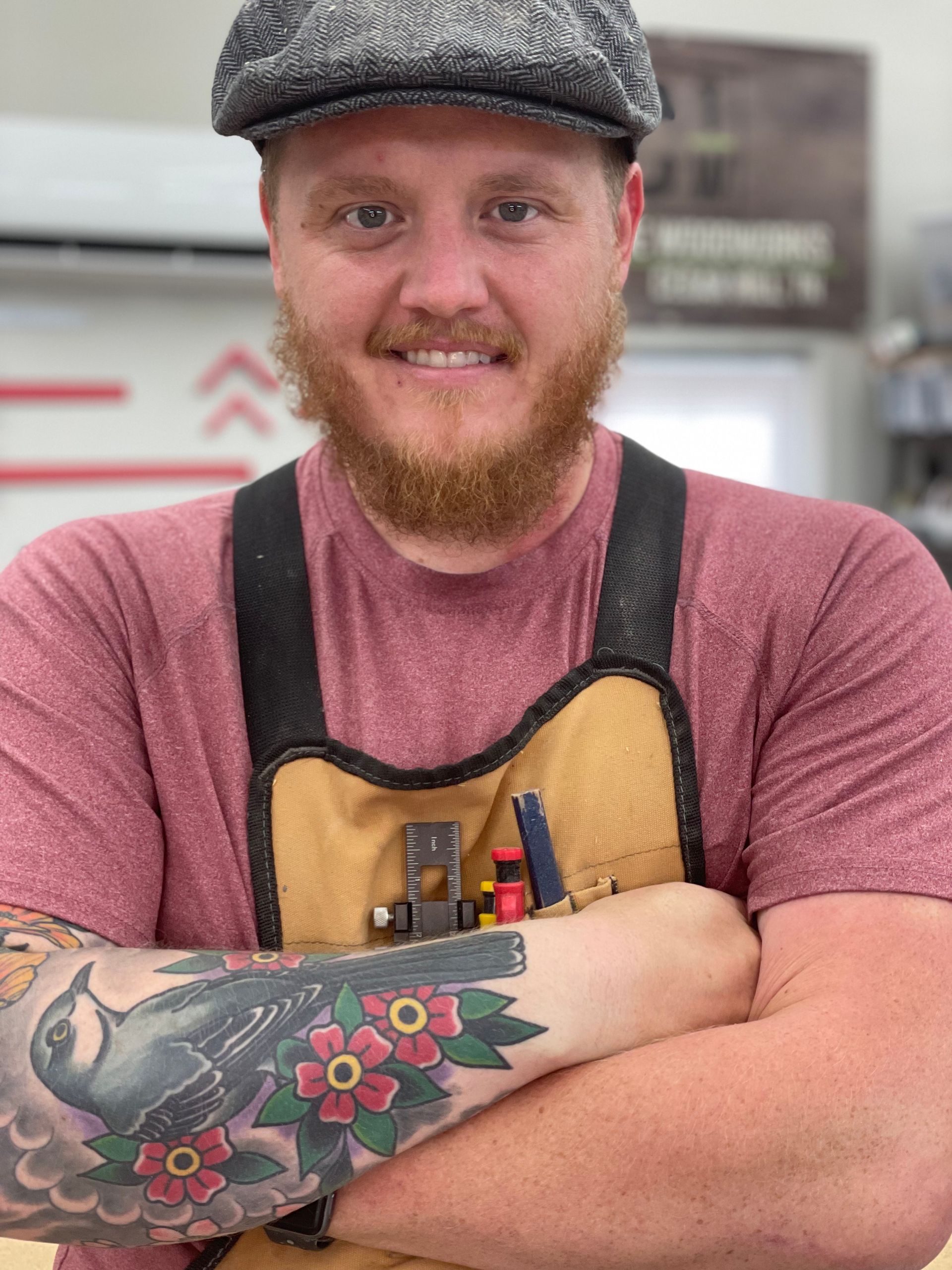 A man with a beard and a tattoo on his arm is wearing a hat and apron.