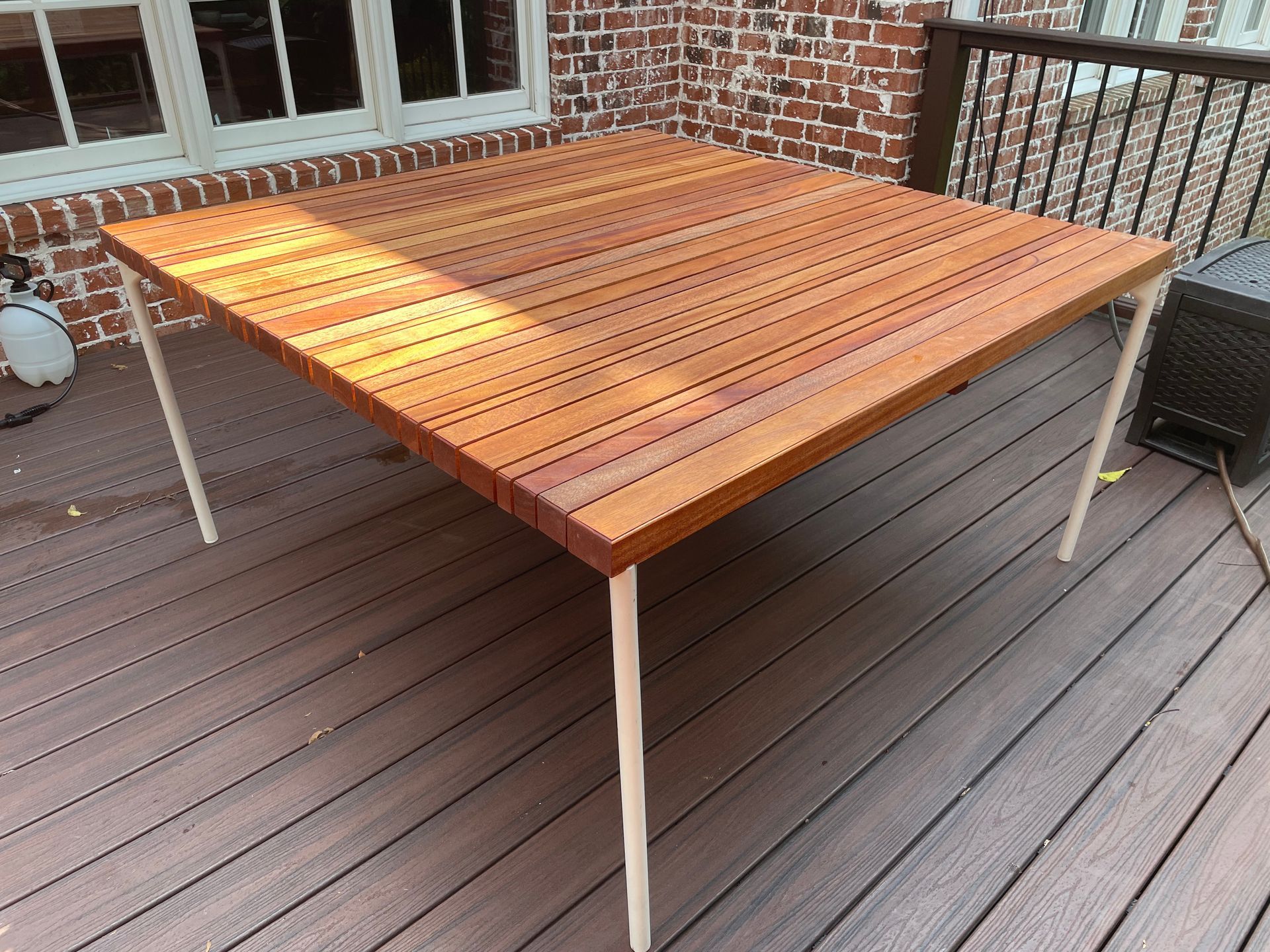 A wooden table is sitting on a wooden deck in front of a brick building.