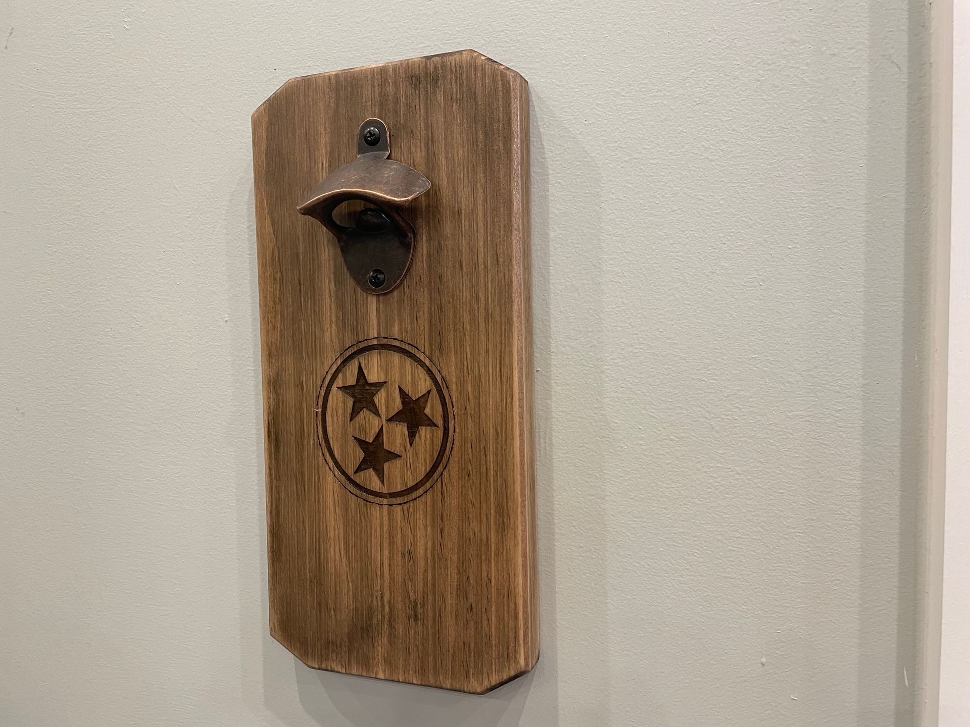 A wooden bottle opener is hanging on a wall.