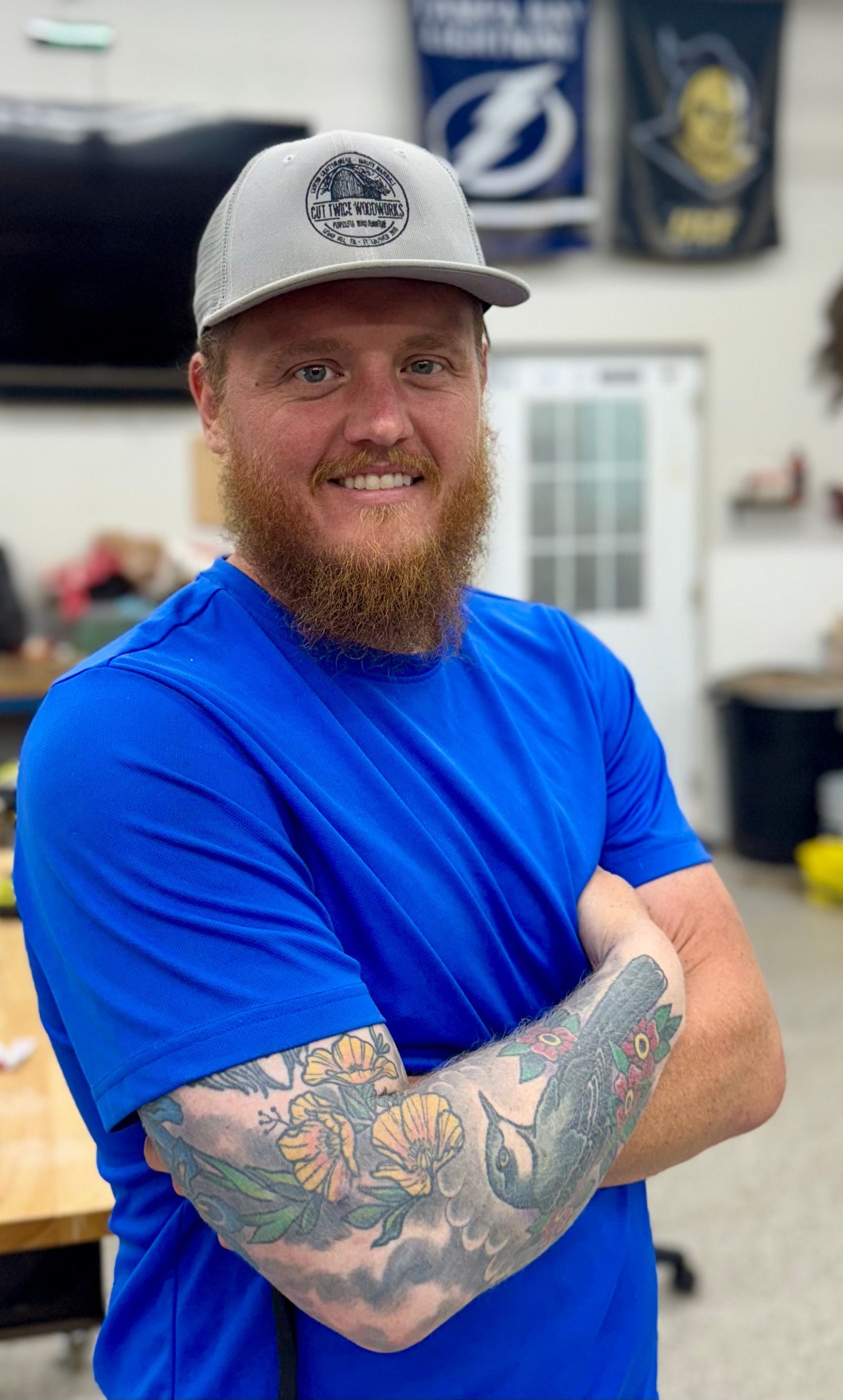 A man with a beard and a tattoo on his arm is wearing a hat and apron.