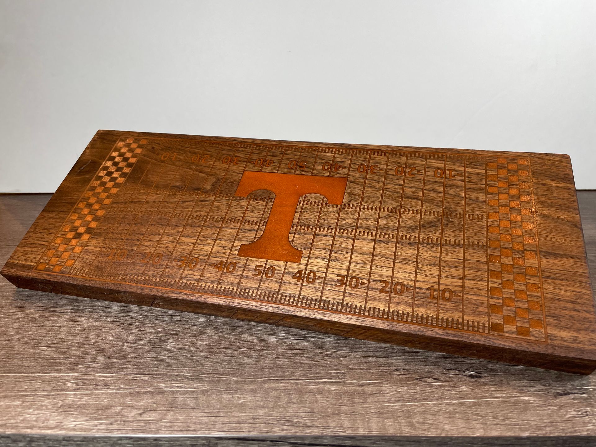A wooden cutting board with the letter t on it is sitting on a table.
