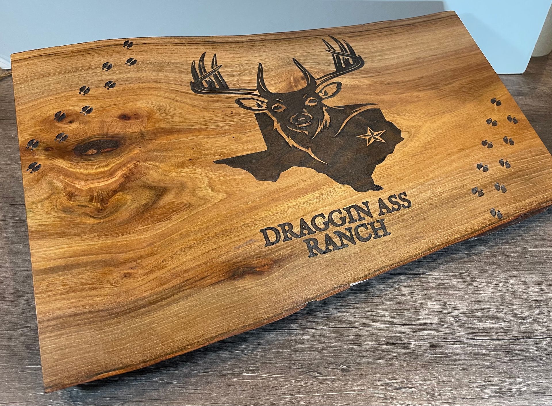 A wooden cutting board with a deer on it is sitting on a wooden table.