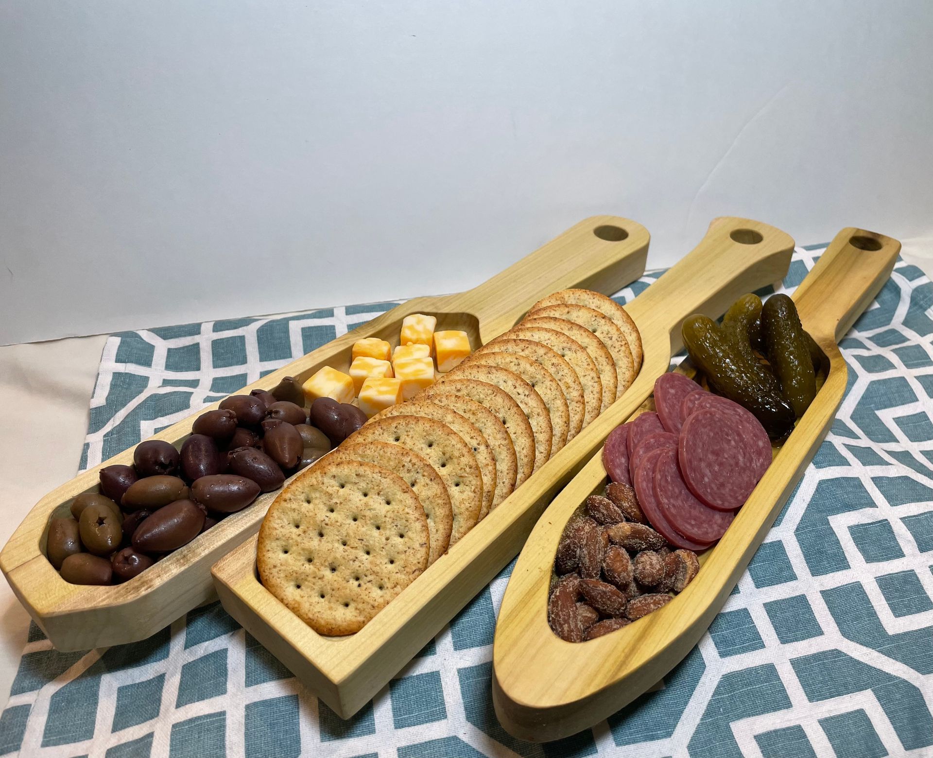 Three wooden spoons filled with crackers , olives , and pickles on a table.
