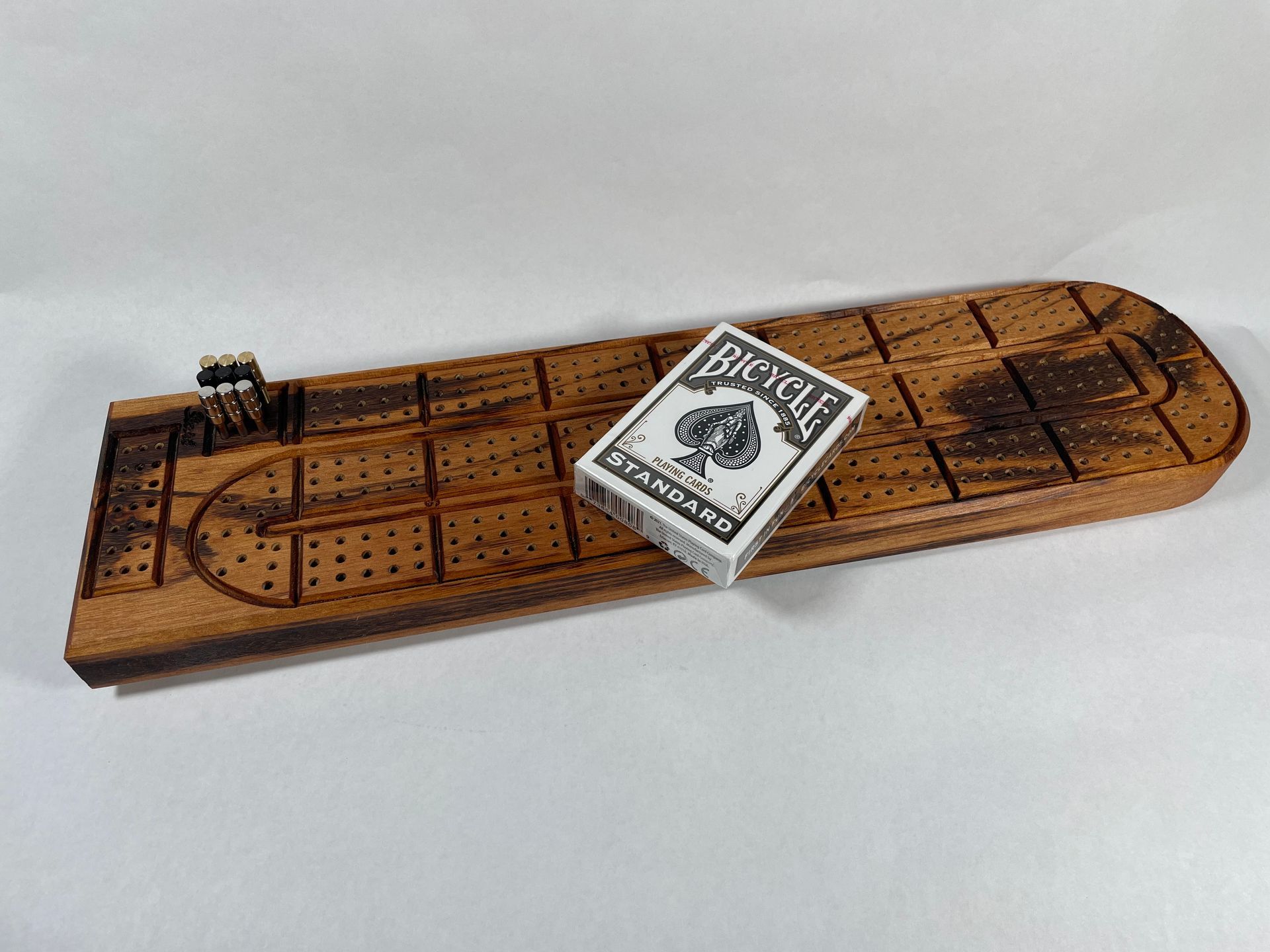 A bicycle playing card is sitting on top of a wooden cribbage board.