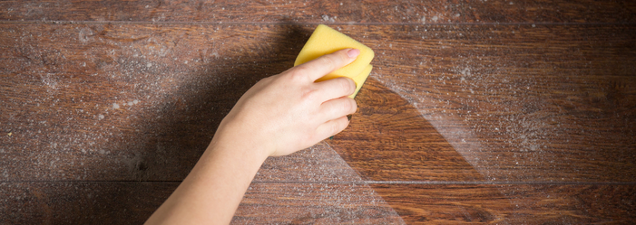 A person is cleaning a wooden table with a yellow sponge.