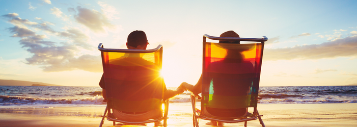 A man and a woman are sitting in beach chairs on the beach holding hands.