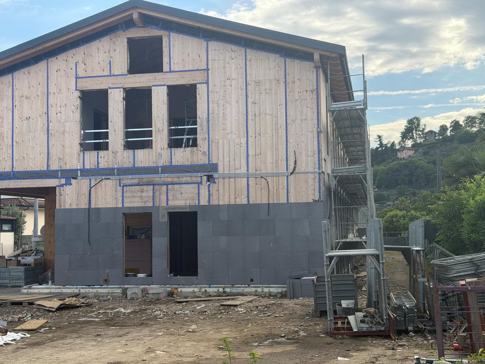 Casa a due piani parzialmente ristrutturata con rivestimento esterno a vista, impalcature e detriti davanti.