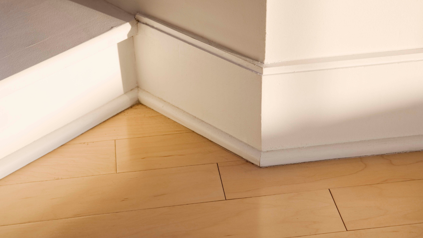 White baseboard molding at corner of walls and light wood floor.