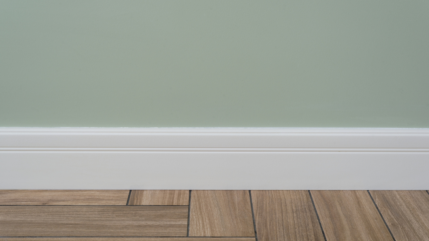 Light green wall with white baseboard above wood-look floor.