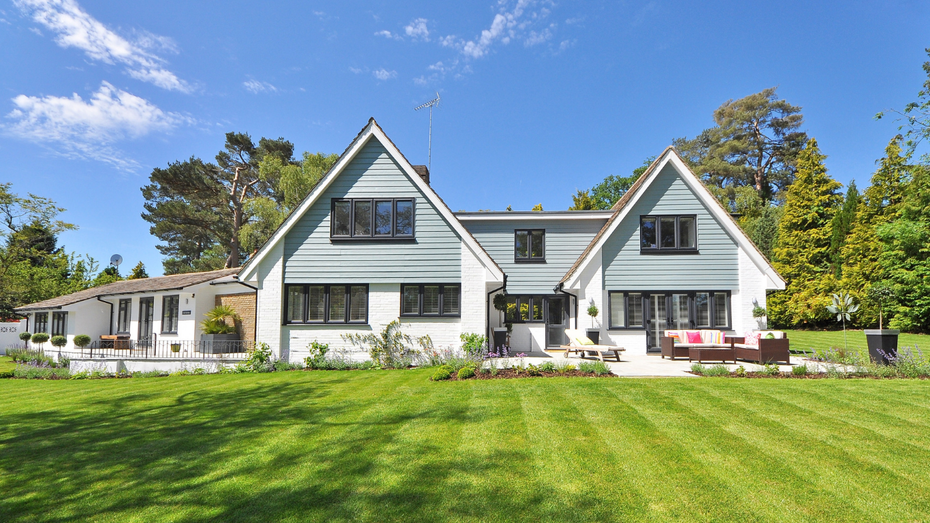 A two-story house with a green lawn under a blue sky. The house has white walls, blue trim, and dark windows.