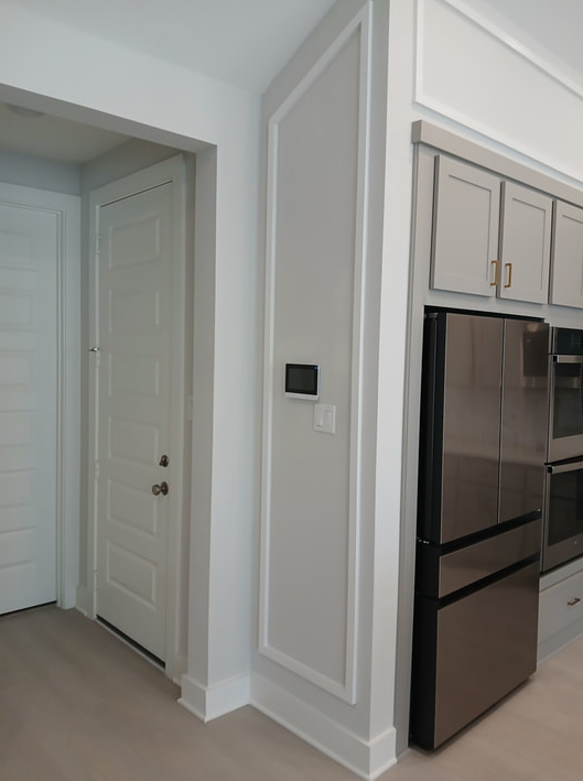 Entryway with a white door, grey wall with white trim, and a refrigerator.