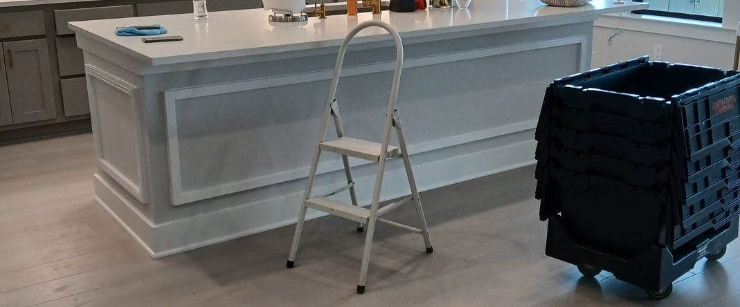 A kitchen island with a stepladder and a rolling bin on the floor.