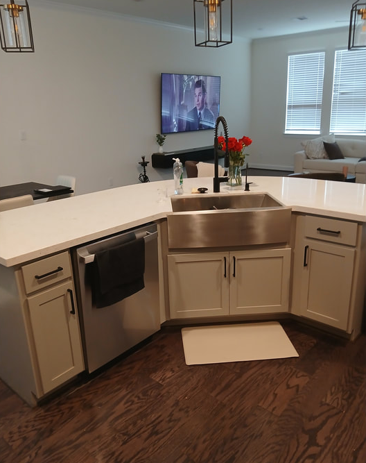 Modern kitchen with white cabinets, stainless steel sink, and TV on wall.