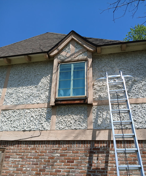 A ladder next to a stucco house with a window under a triangular roof. Blue sky in the background.