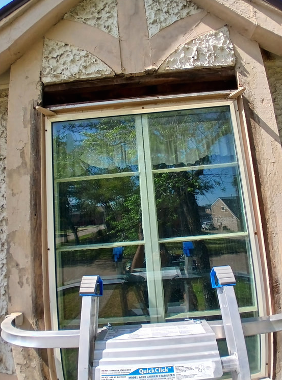 Window with wood trim and stucco facade; ladder in front.