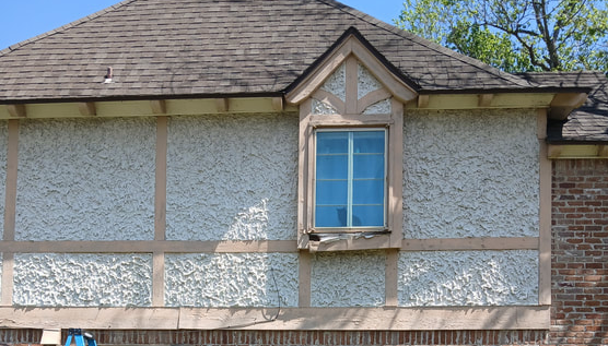 A white stucco building with brown trim, a window, and a dark shingle roof.