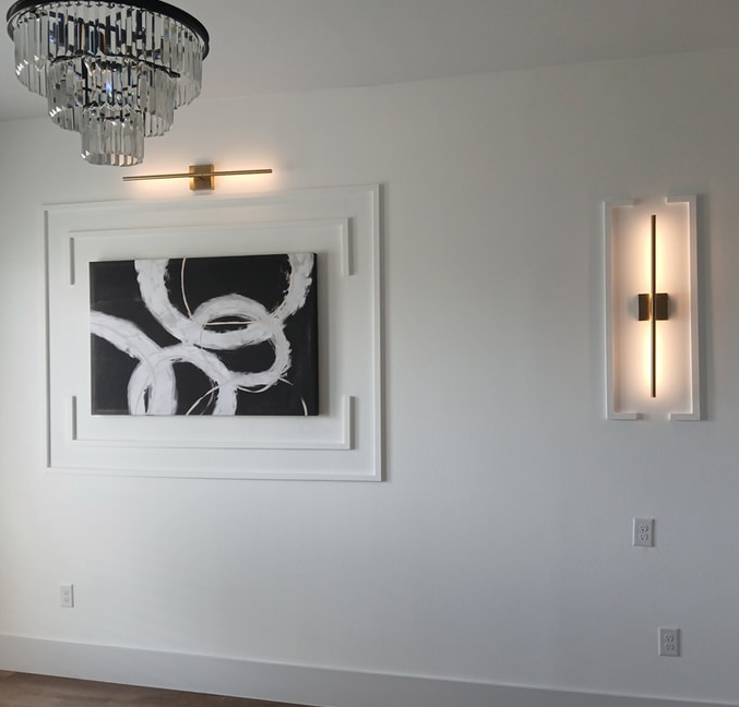 White room with art and sconces, including a black and white abstract painting.