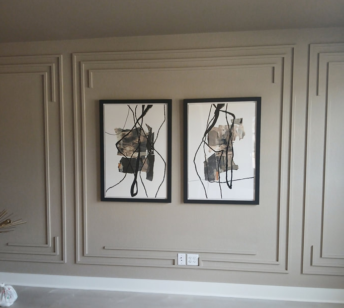 Two framed abstract paintings hang on a wall with beige paneling.