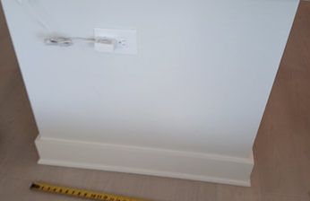 White wall with baseboard, electrical outlet, and a tape measure on the floor.