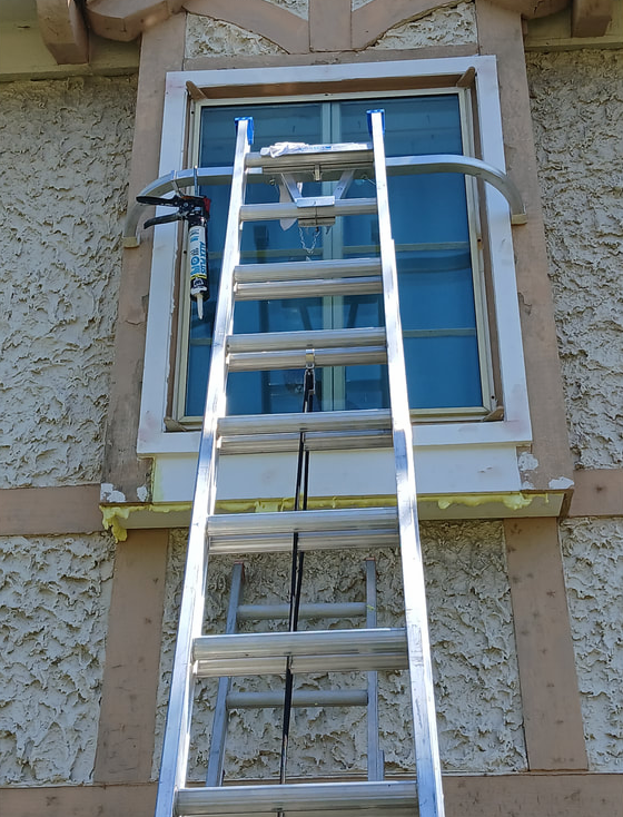 Ladder leaning against a window; worker is repairing the exterior stucco of a house.