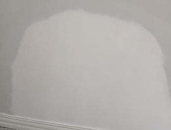 Patch of white paint on a wall above a baseboard, the patch is lighter than the surrounding wall.
