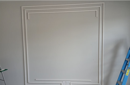 A wall with white trim in a square design, blue ladder on the right.