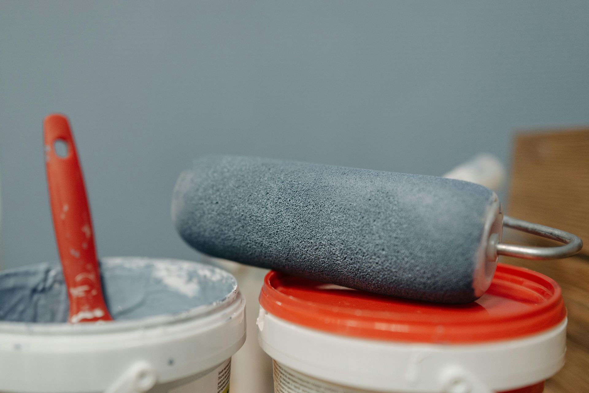 Paint roller on a paint can with a red handle in a blue-painted setting.