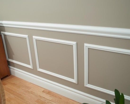 White wainscoting with rectangular panels on a beige wall. Wooden floor and white crown molding.
