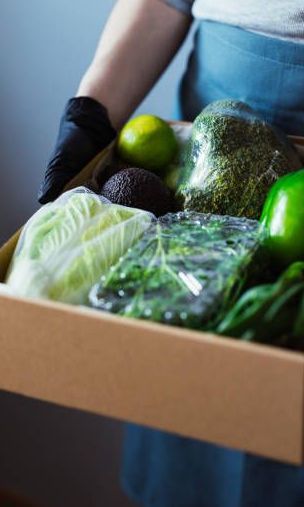 A person is holding a cardboard box filled with vegetables.
