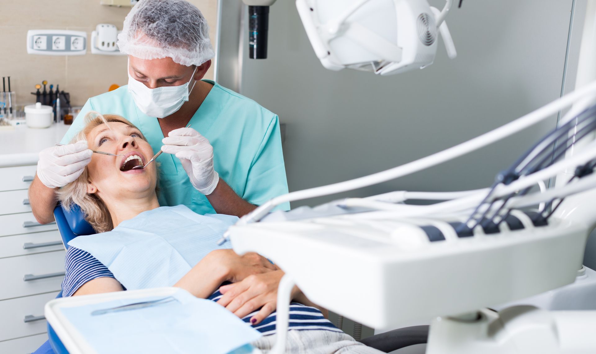 A woman is sitting in a dental chair while a dentist examines her teeth.