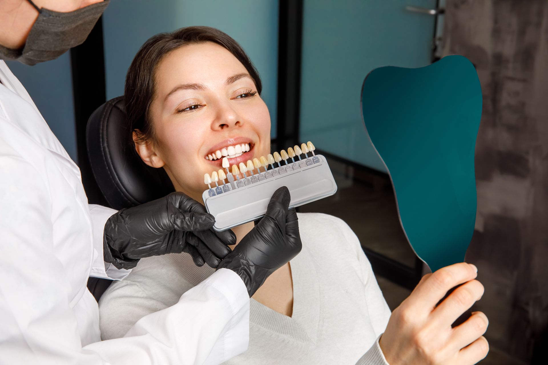 A woman is sitting in a dental chair looking at her teeth in a mirror.