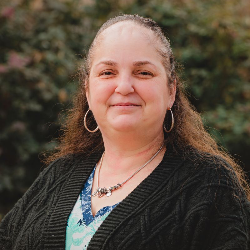 An elderly woman wearing glasses and a sweater is smiling for the camera.