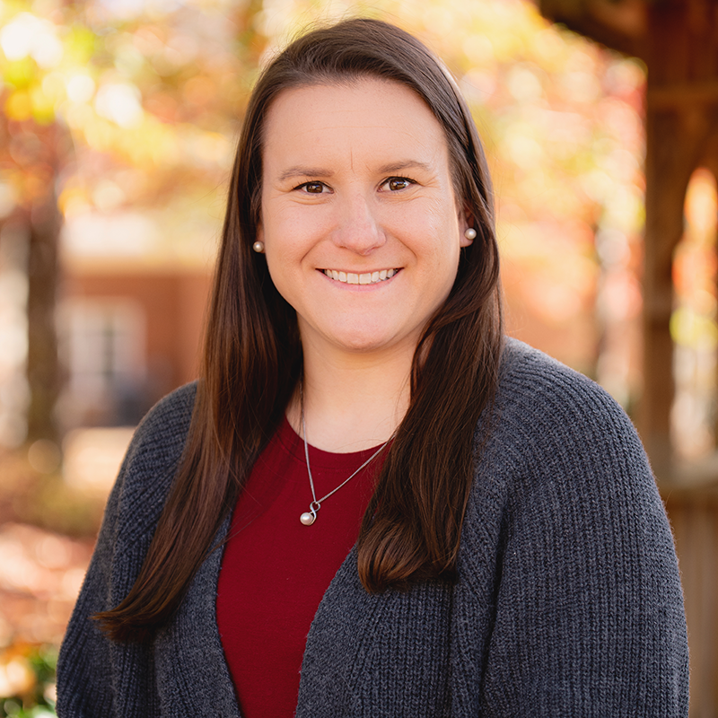 A woman wearing a grey sweater and a red shirt is smiling for the camera.
