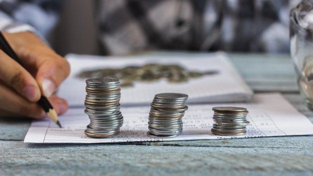 A person is writing on a piece of paper next to stacks of coins.