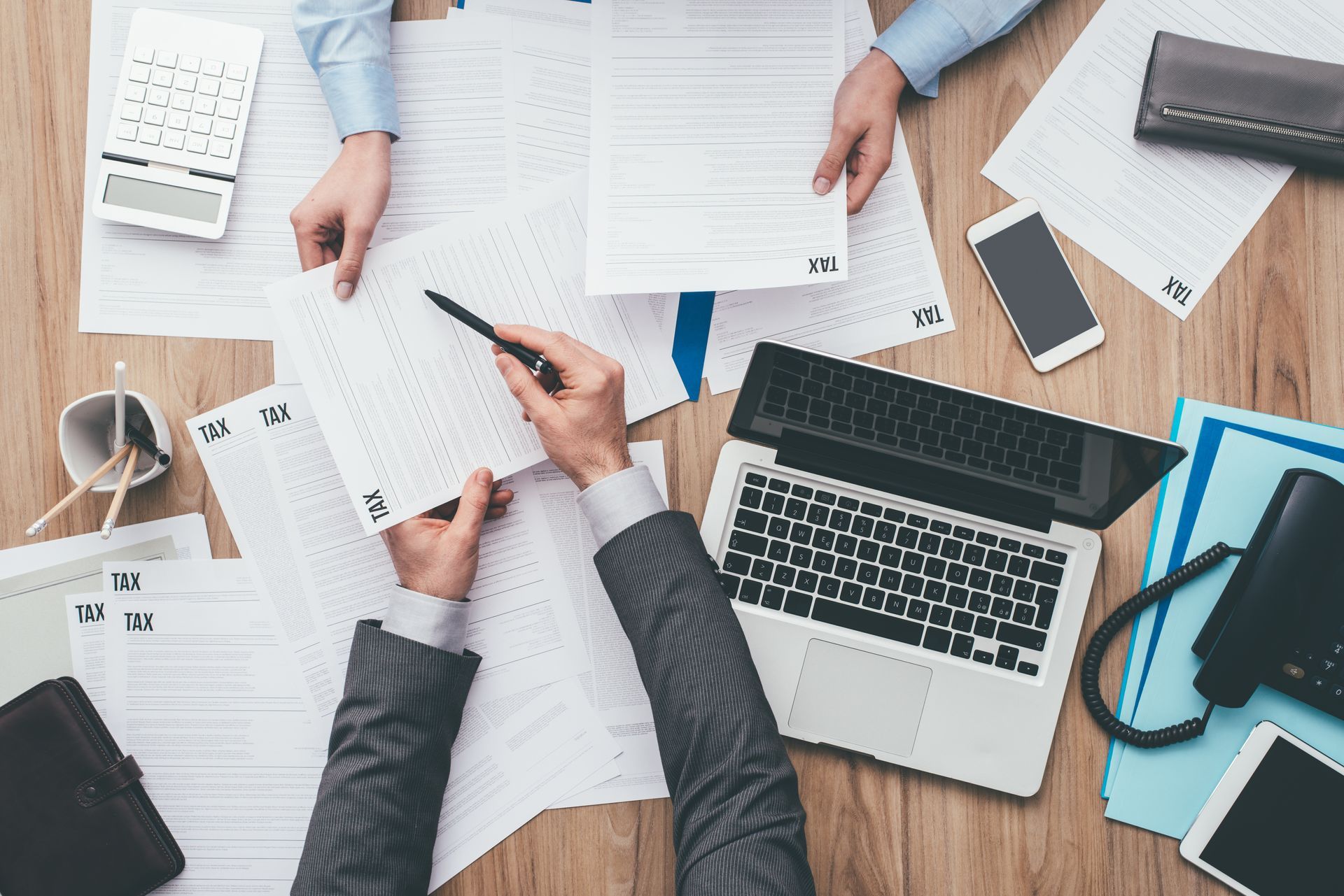 Business partners checking tax forms with laptop, phone, and calculator on a wooden desk.