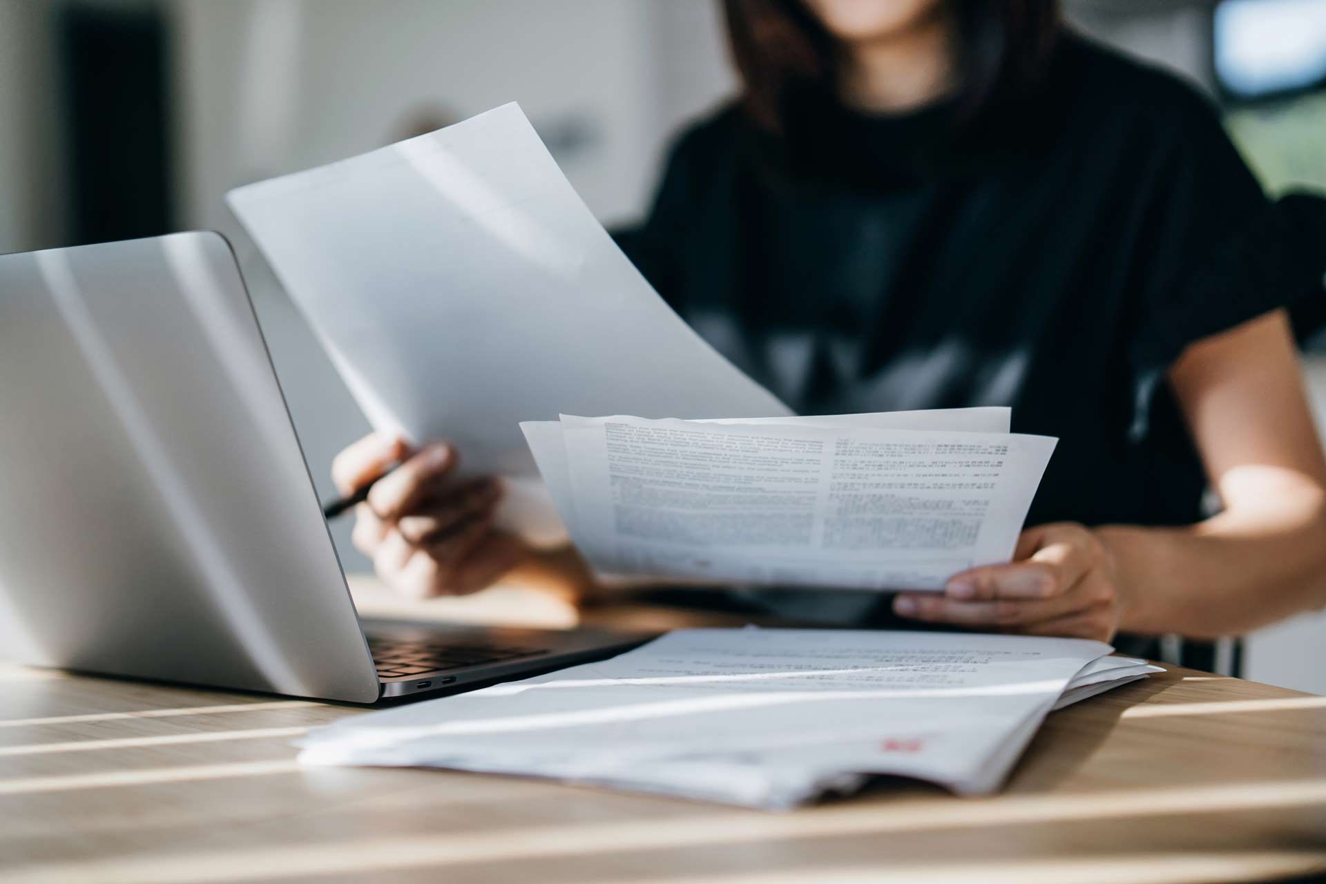 Person reviewing documents at a desk with a laptop.
