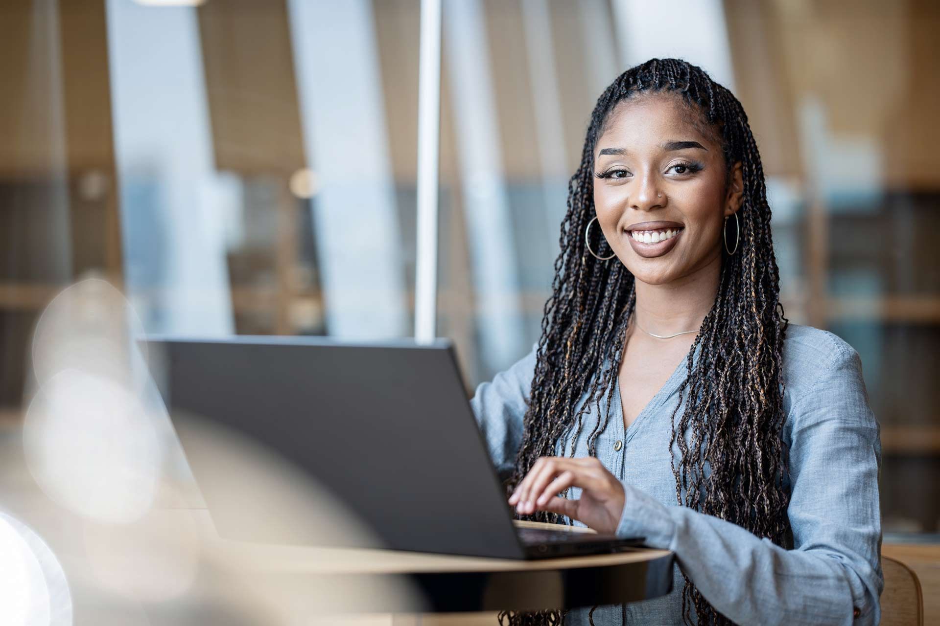 Person with braided hair working on a laptop in a bright indoor office setting.