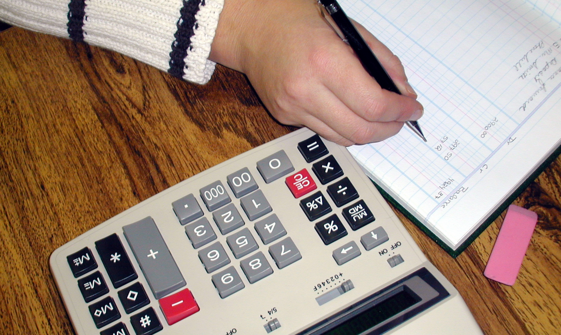 A person is using a calculator and writing in a notebook
