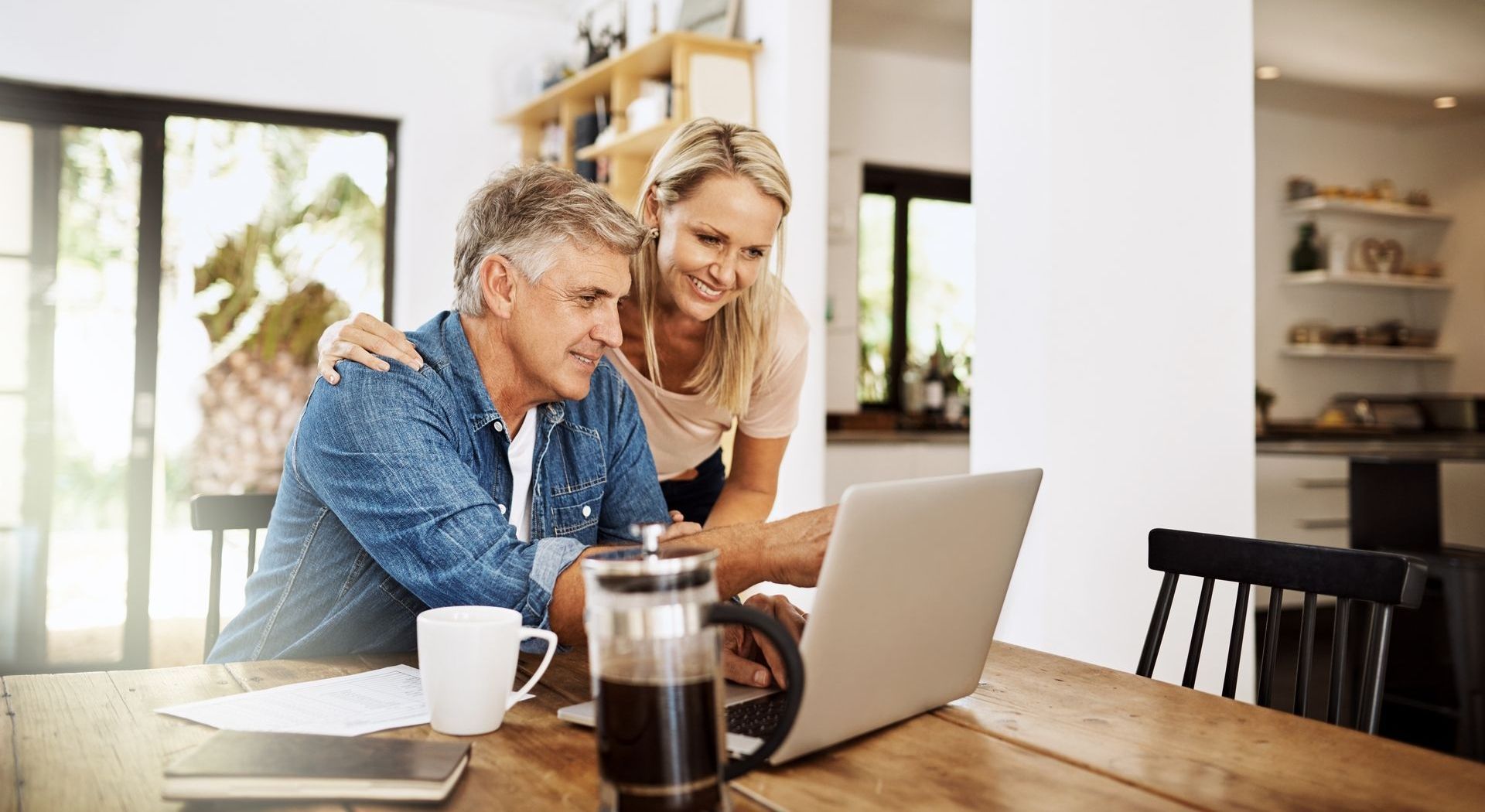 A man and a woman are sitting at a table looking at a laptop computer.