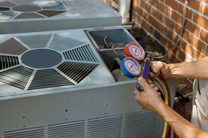 A man is working on an air conditioner outside of a brick building