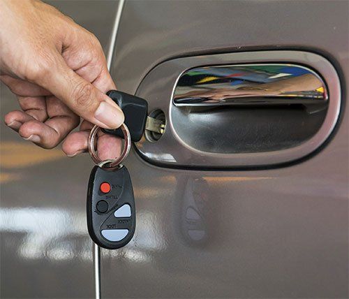 A person is holding a car key in front of a car door.