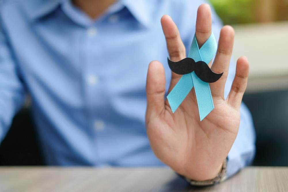 Man is Holding a Blue Ribbon With a Fake Mustache on His Finger — Mullumbimby Comprehensive Health Centre in Mullumbimby, NSW