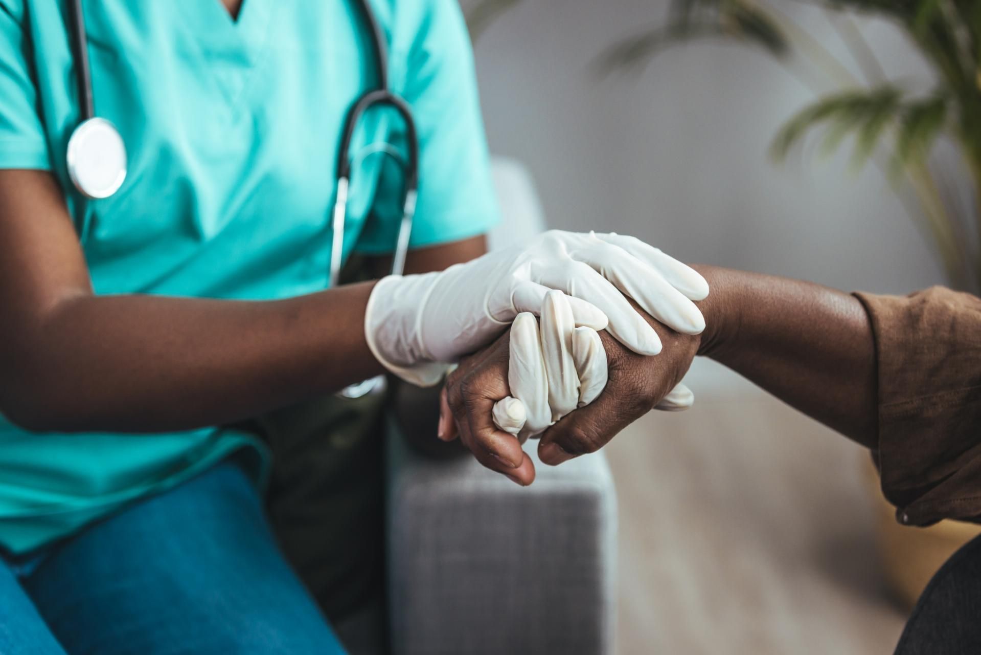Nurse is Holding a Patient 's Hand While Wearing Gloves — Mullumbimby Comprehensive Health Centre in Mullumbimby, NSW