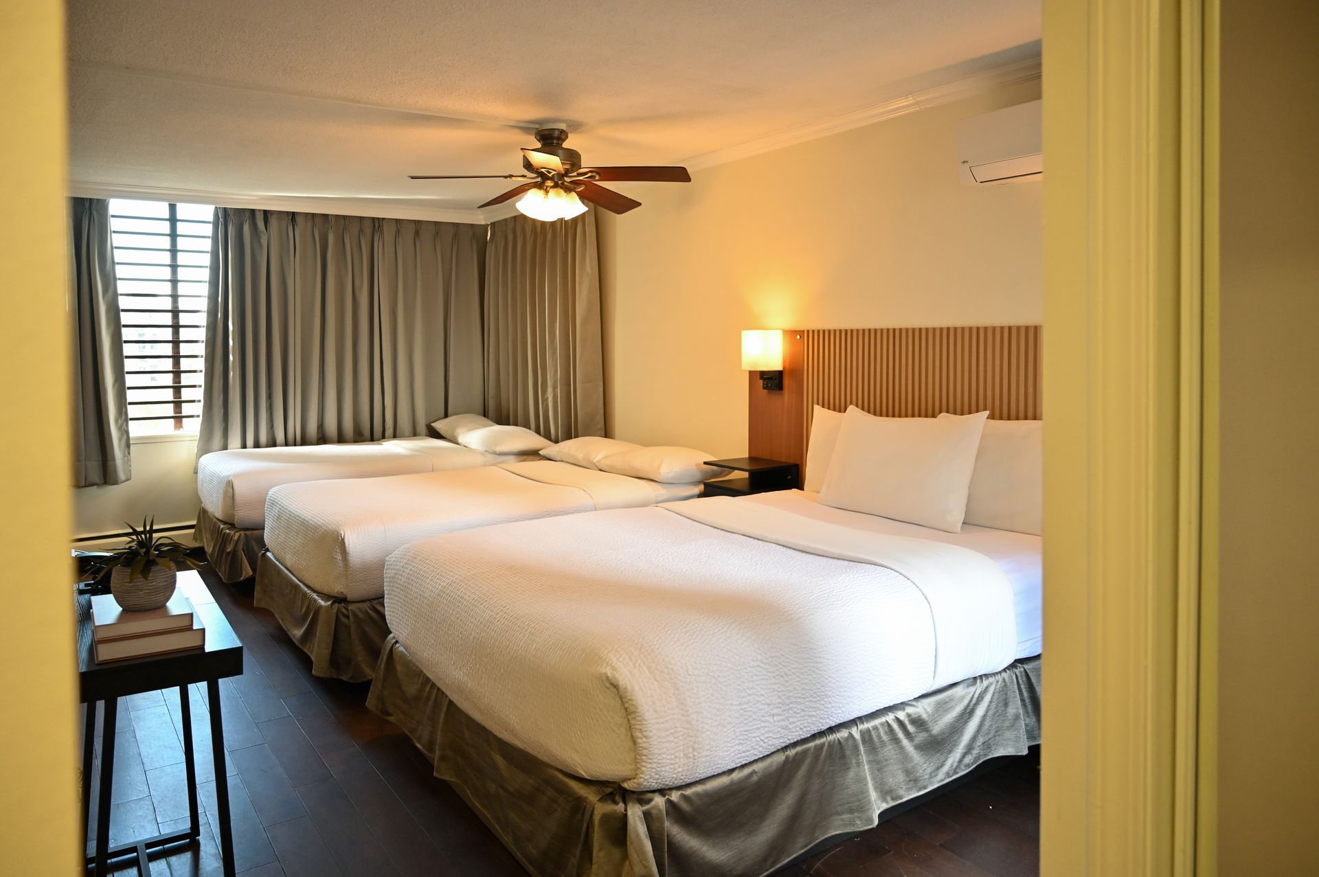 A hotel room with two white beds, neutral-toned bedding, floor-to-ceiling curtains, and a ceiling fan.