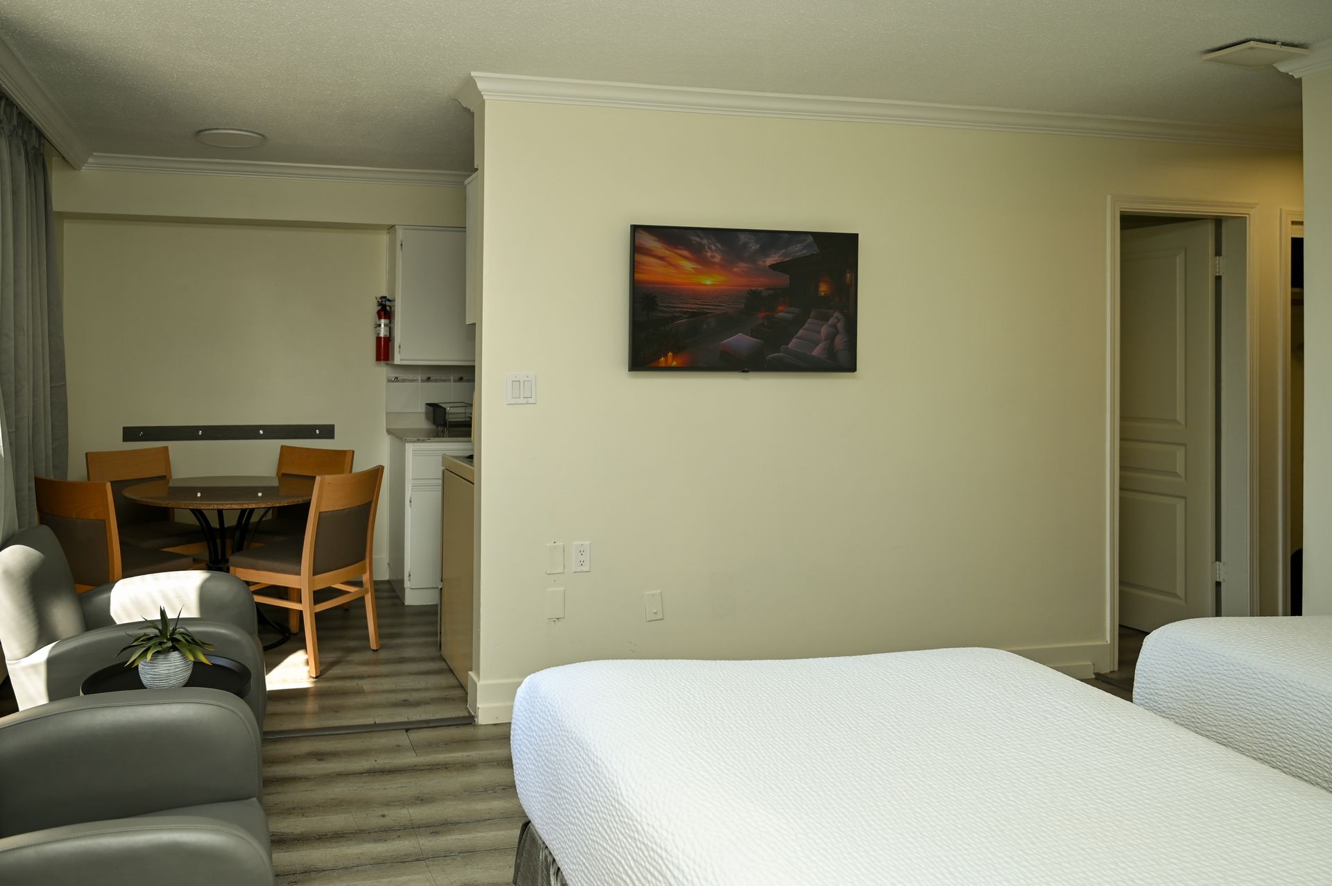 A hotel room with two beds, a dining table and chairs, and a television mounted on a central light-colored wall.