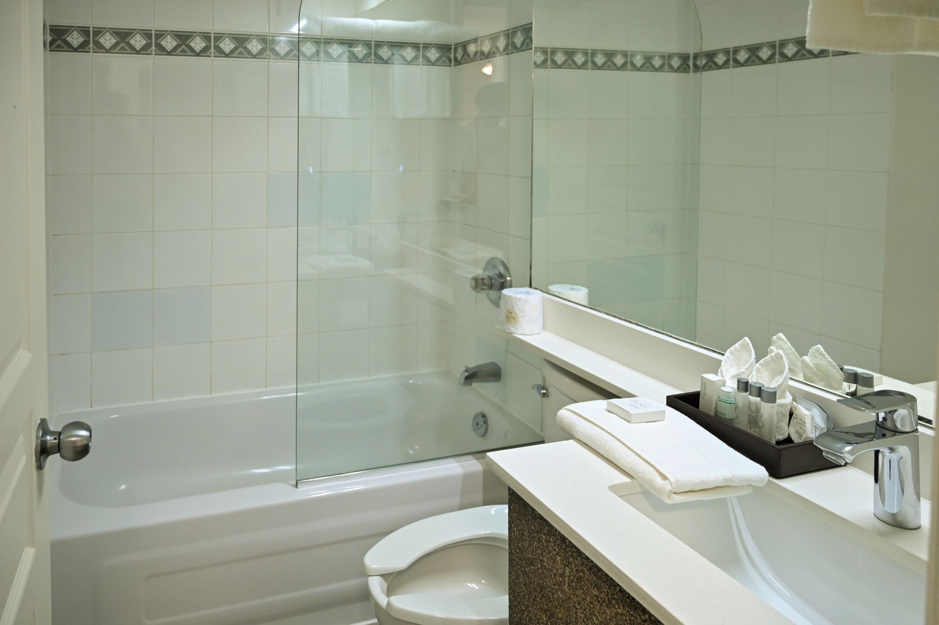 A bright bathroom featuring a white bathtub, a glass shower partition, a toilet, and a vanity sink with toiletries.