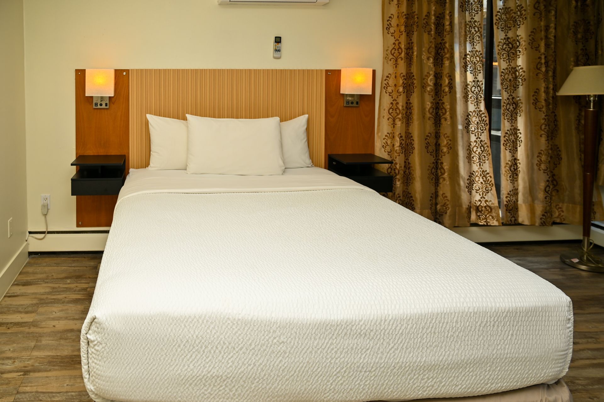 A hotel room featuring a bed with white bedding, wooden headboard, side tables with lamps, and gold curtains.