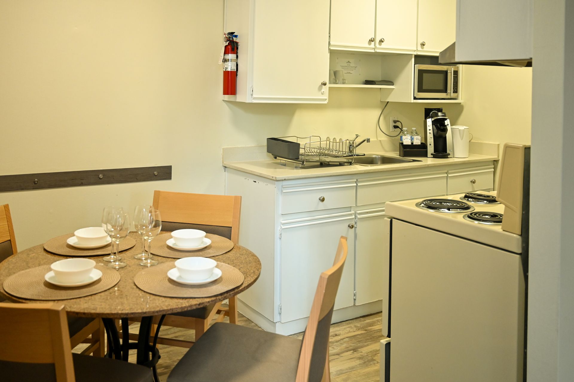 A small dining area with a round table set for four next to a compact kitchen featuring white cabinets and appliances.