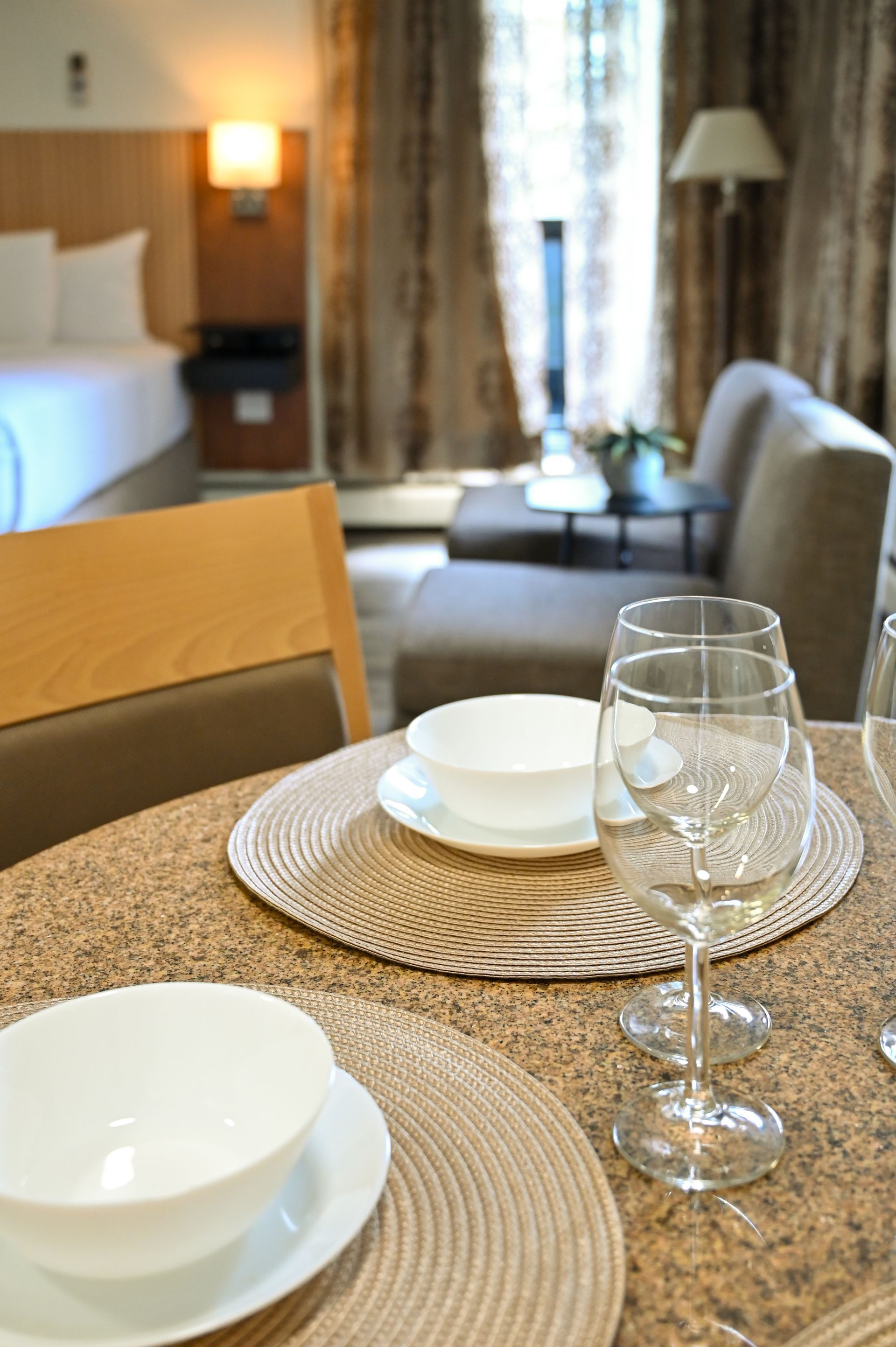 A close-up of a table setting with white bowls and glasses, with a blurred hotel room in the background.
